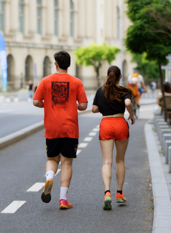 15 - Two individuals running outdoors on a paved path, wearing vibrant orange and black activewear